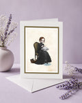 An alternative art greeting card featuring a dark whimsy pop surrealism illustration of a girl knitting a raincloud while sitting on a vintage chair, standing upright on its white envelope next to a ceramic vase with dried lavender on a purple background.
