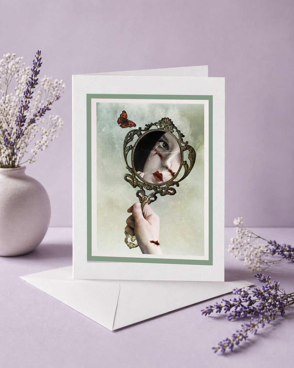 Gothic mirror art greeting card with white envelope, displayed open and ready to frame next to dried lavender. The surreal artwork features a vintage mirror reflection, a butterfly, and dark fantasy imagery.