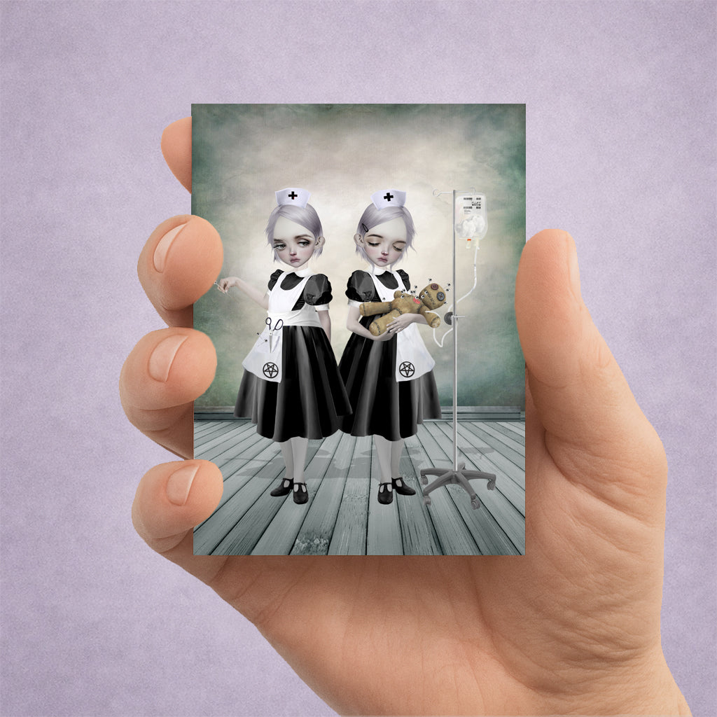 Hand holding an ACEO print of two gothic nurses holding a voodoo doll
