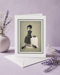 An alternative art greeting card featuring a dark whimsy pop surrealism illustration of a girl on a giant sugar cube with large ants, standing upright on its white envelope next to a ceramic vase with dried lavender on a purple background.