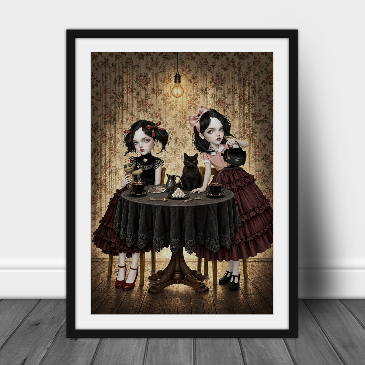 Gothic Tea Party Art Print in an A3 frame featuring two gothic girls sitting at a round wooden table having a tea party with a black cat, a voodoo doll, and tarot cards.