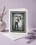Greeting card with a framed illustration of gothic vampire couple forever young on a purple background with flowers.