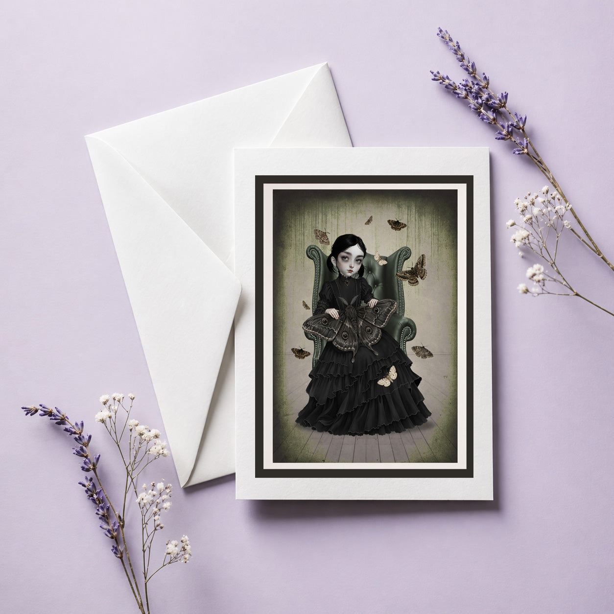 Art greeting card and envelope featuring a gothic girl with moths sitting in an armchair, displayed next to dried lavender flowers.