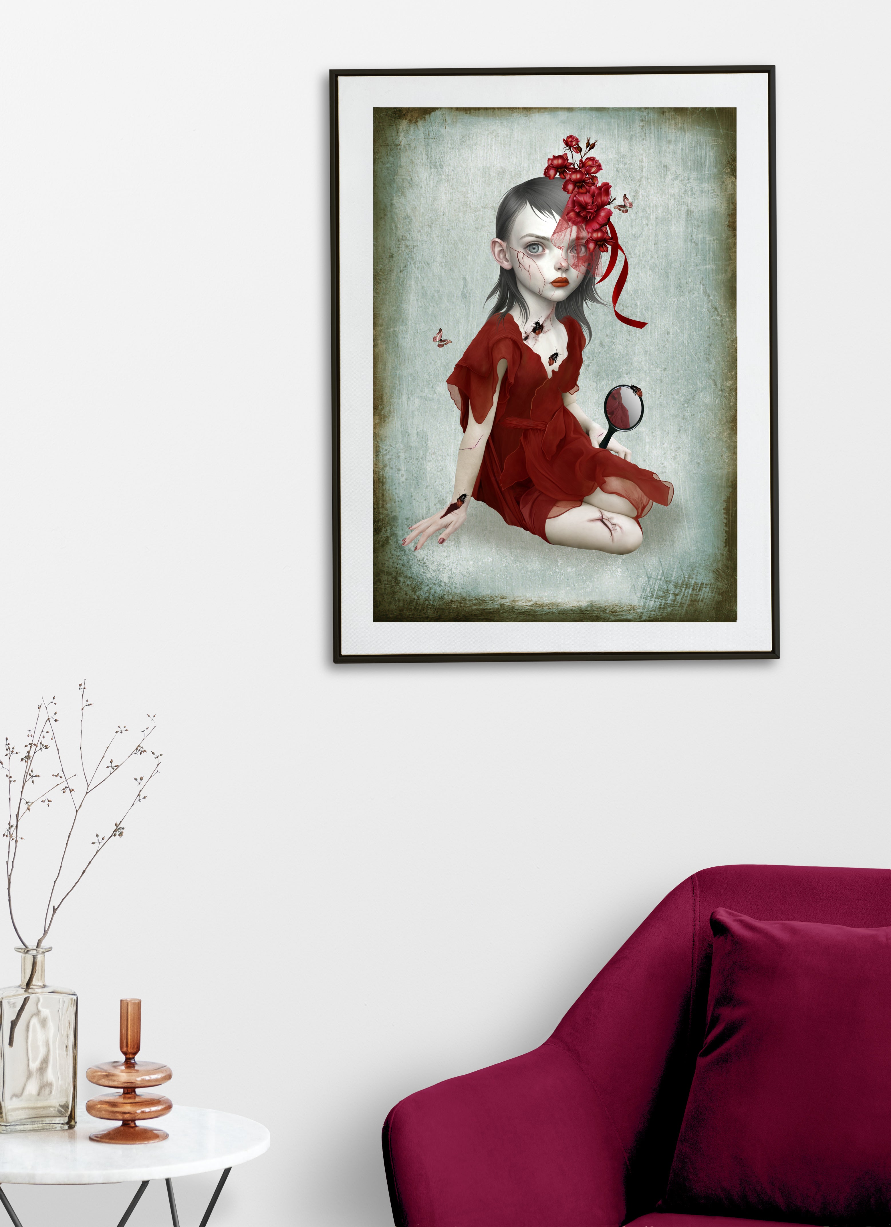 Framed artwork of a girl in a red dress with a floral headpiece and hand mirror on a white wall above a maroon sofa.