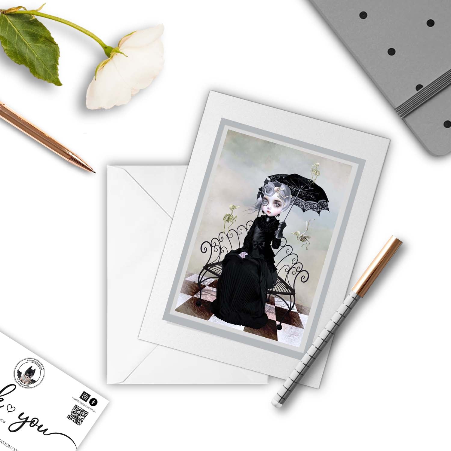 Mockup of Gothic victorian lady and skeletal birds greeting card, with a pen and other stationery items arranged around it