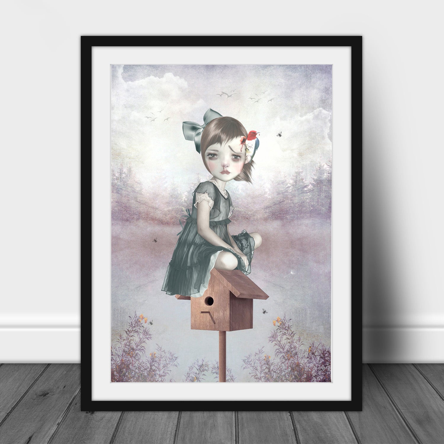Large black-framed surreal art print of a girl sitting on a birdhouse with a woodpecker pecking her head, leaning against a wall for a bold, artistic display.