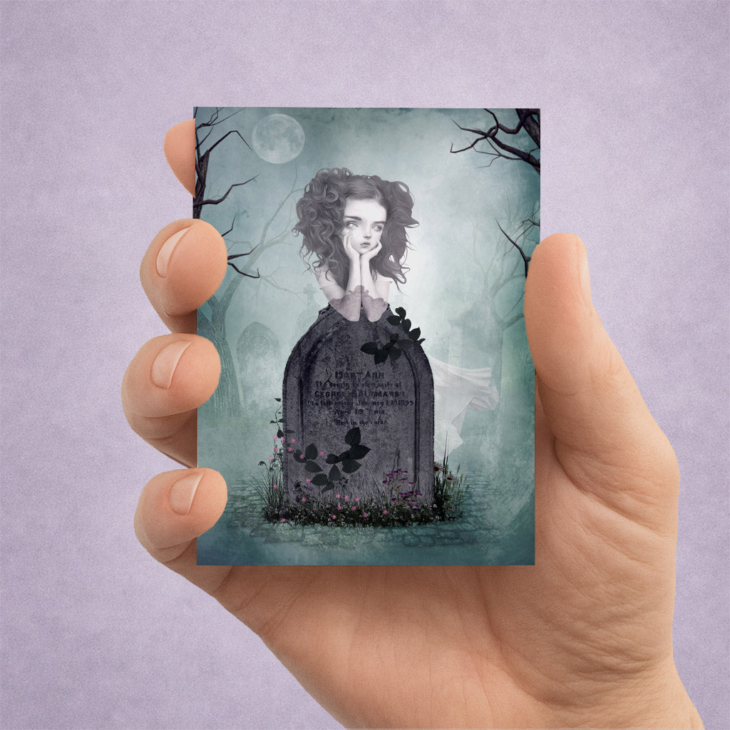 Hand holding an ACEO card with a gothic design of a ghost girl by her tombstone against a purple background.