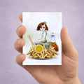 Hand holding an ACEO card with an illustration of a sad mermaid among chips, lemon, sitting on a diners plate.
