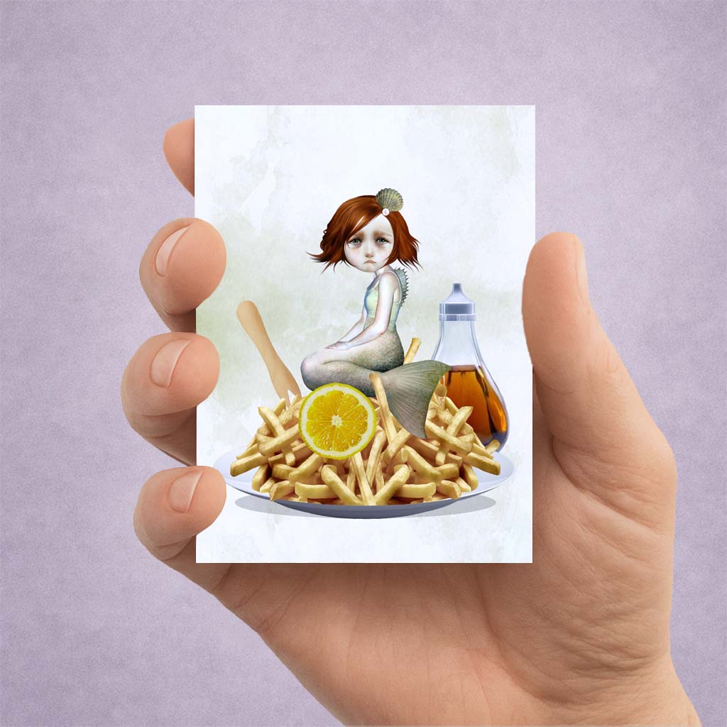 Hand holding an ACEO card with an illustration of a sad mermaid among chips, lemon, sitting on a diners plate.
