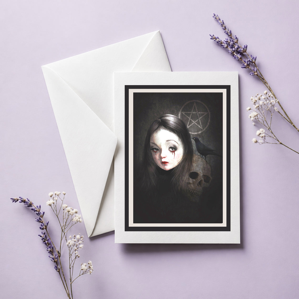 The Occultist dark gothic greeting card with white envelope, featuring a skull, blackbird, weeping girl, and pentacle laid on a lilac background.