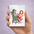 Hand holding an ACEO card with an illustration of an octopus girl in a chair, with a life buoy, and a rubber duck on a light purple background. 