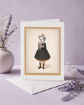 Greeting card with a strange illustration of a girl sipping on a sundae covered in beetles, placed on a light purple surface with decorative elements.