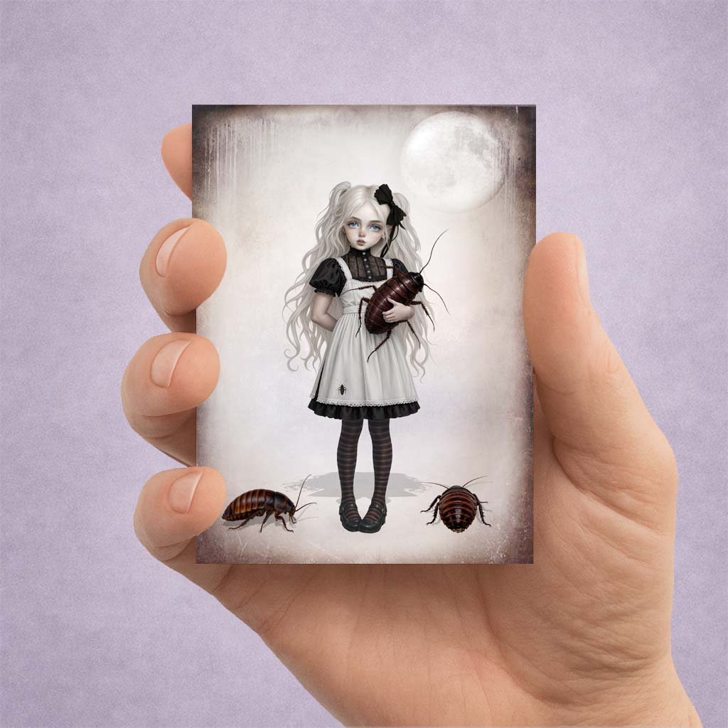 Hand holding a 2.5x3.5 ACEO fine art card of a gothic girl with pigtails holding a giant cockroach under a full moon.