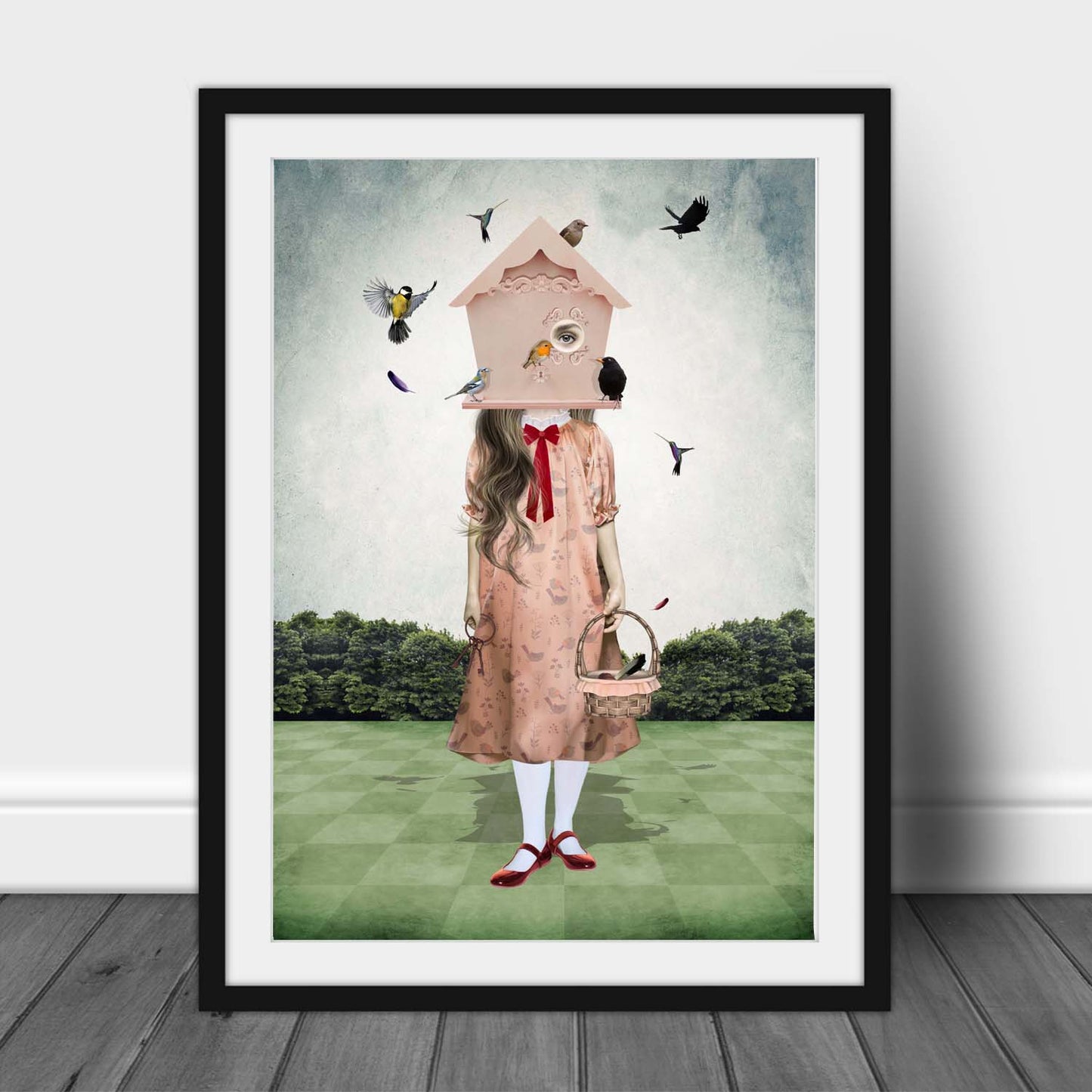 Art print of a quirky girl and garden birds, in a frame, leaned against a wall.