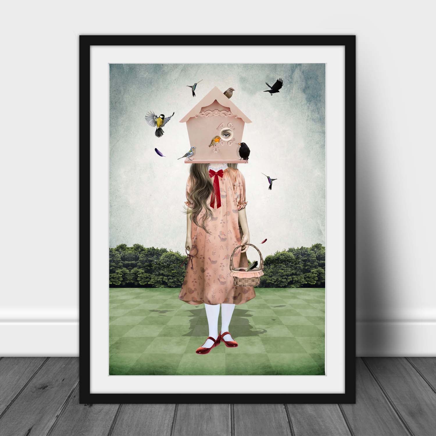 Art print of a quirky girl and garden birds, in a frame, leaned against a wall.