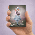 Hand holding an ACEO art card with illustration of a girl holding an oversized rat, displayed on a purple background.
