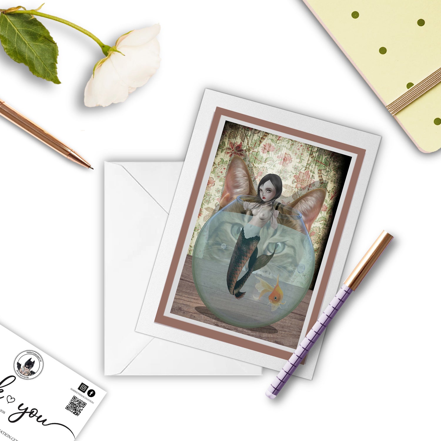 Quirky Mermaid And Cat Art Greeting Card, with a pen and other stationary items arranged around it.