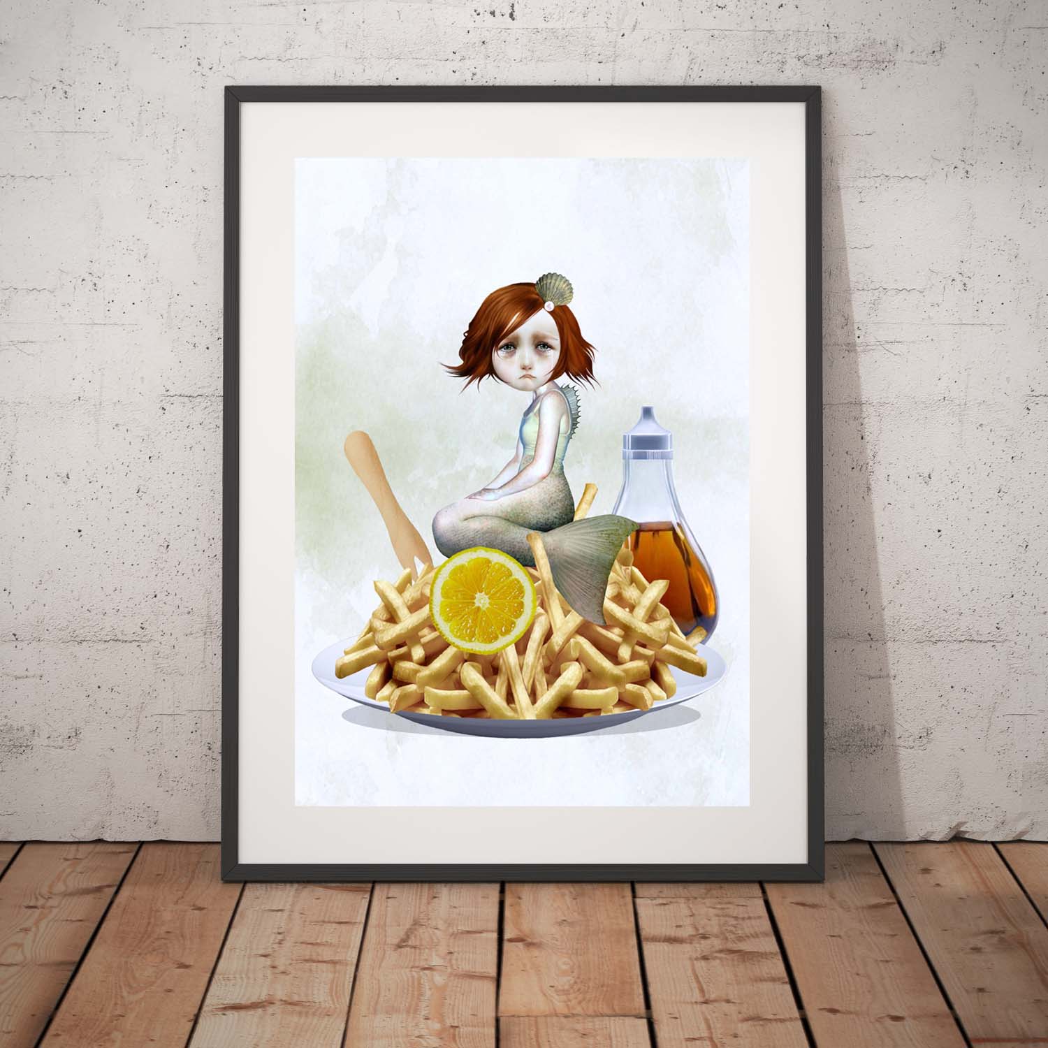 Quirky mermaid art print in a black frame, standing against a white wall.