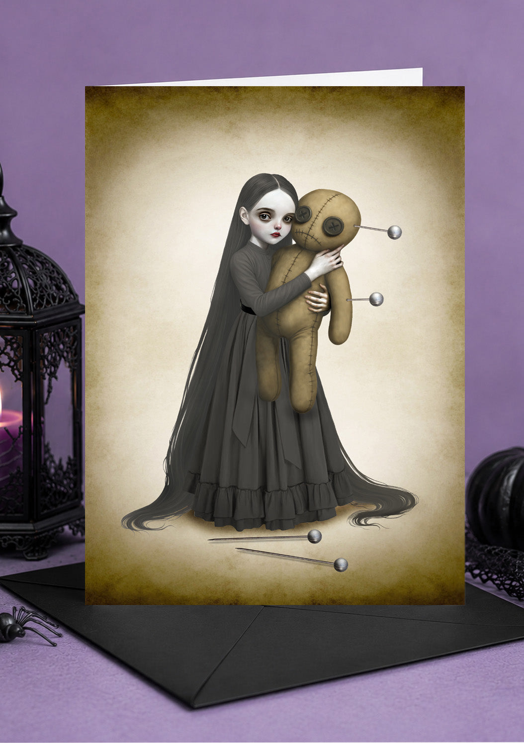 Illustrated card of a long-haired gothic girl in a dark dress hugging a large voodoo doll with pins.