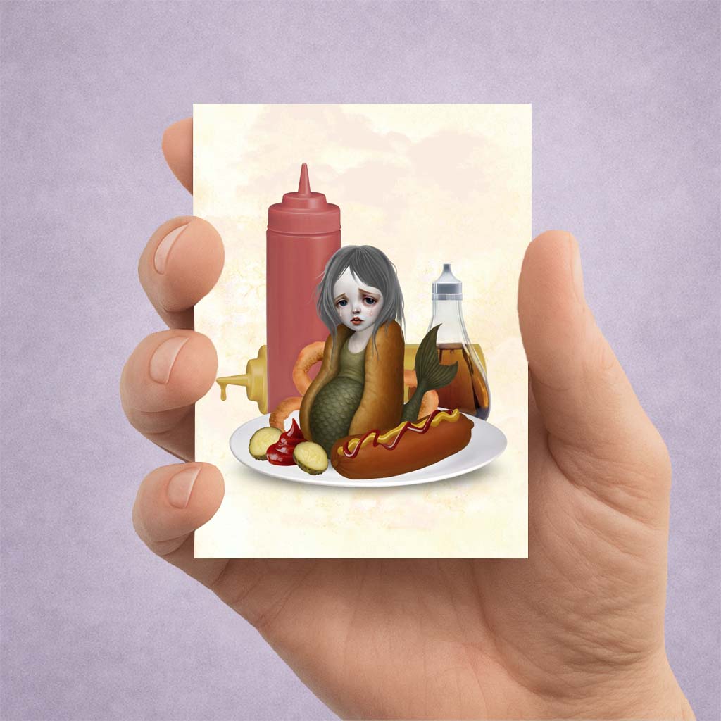 Illustration of a mermaid in an hot dog bun on an ACEO card held by a hand against a light purple background