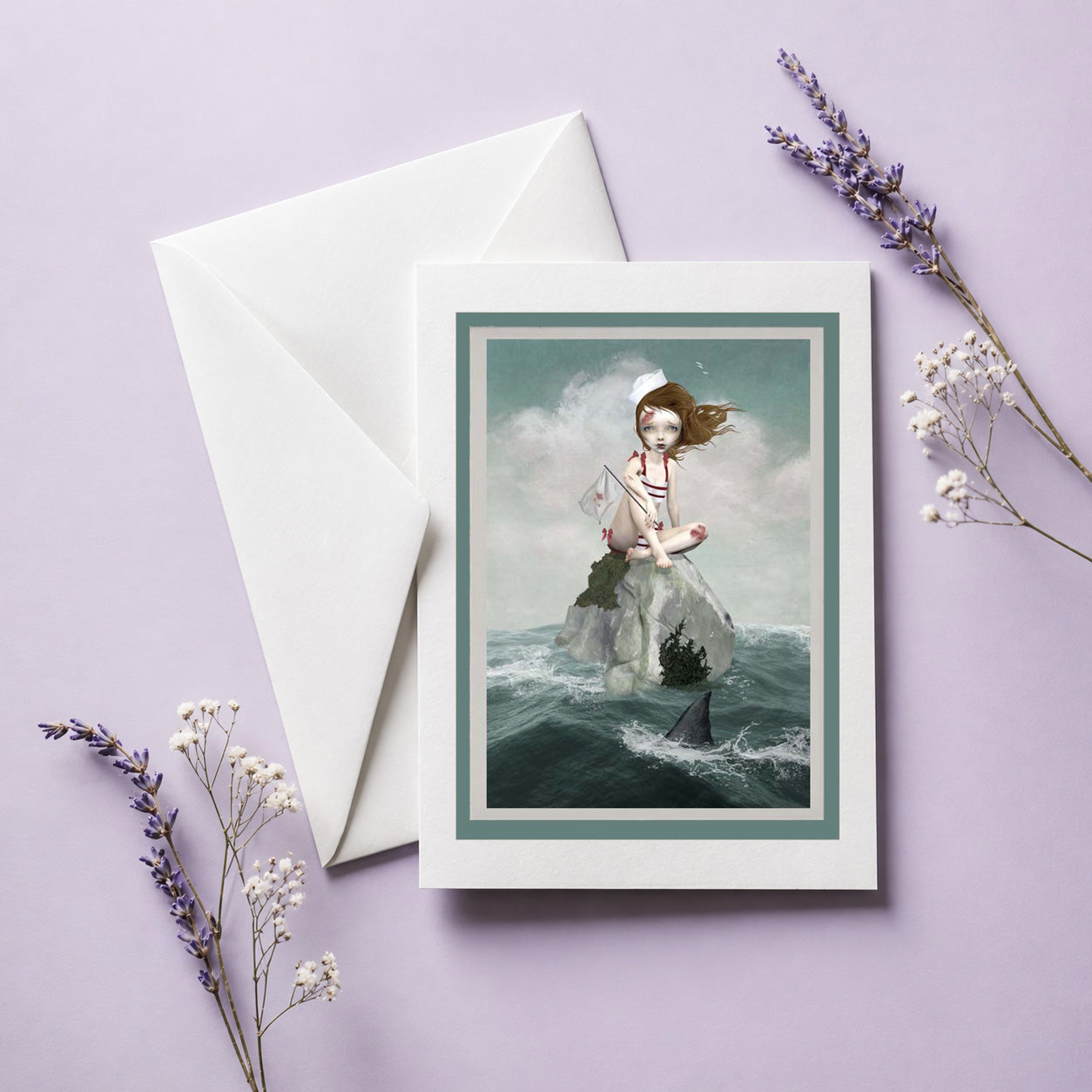 Greeting card with a sailor girl sitting on a rock stranded in the middle of the ocean, envelope, and lavender flowers on a light purple background