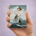 maritime pop surrealism features a wounded sailor girl stranded at sea with shark fin visible.