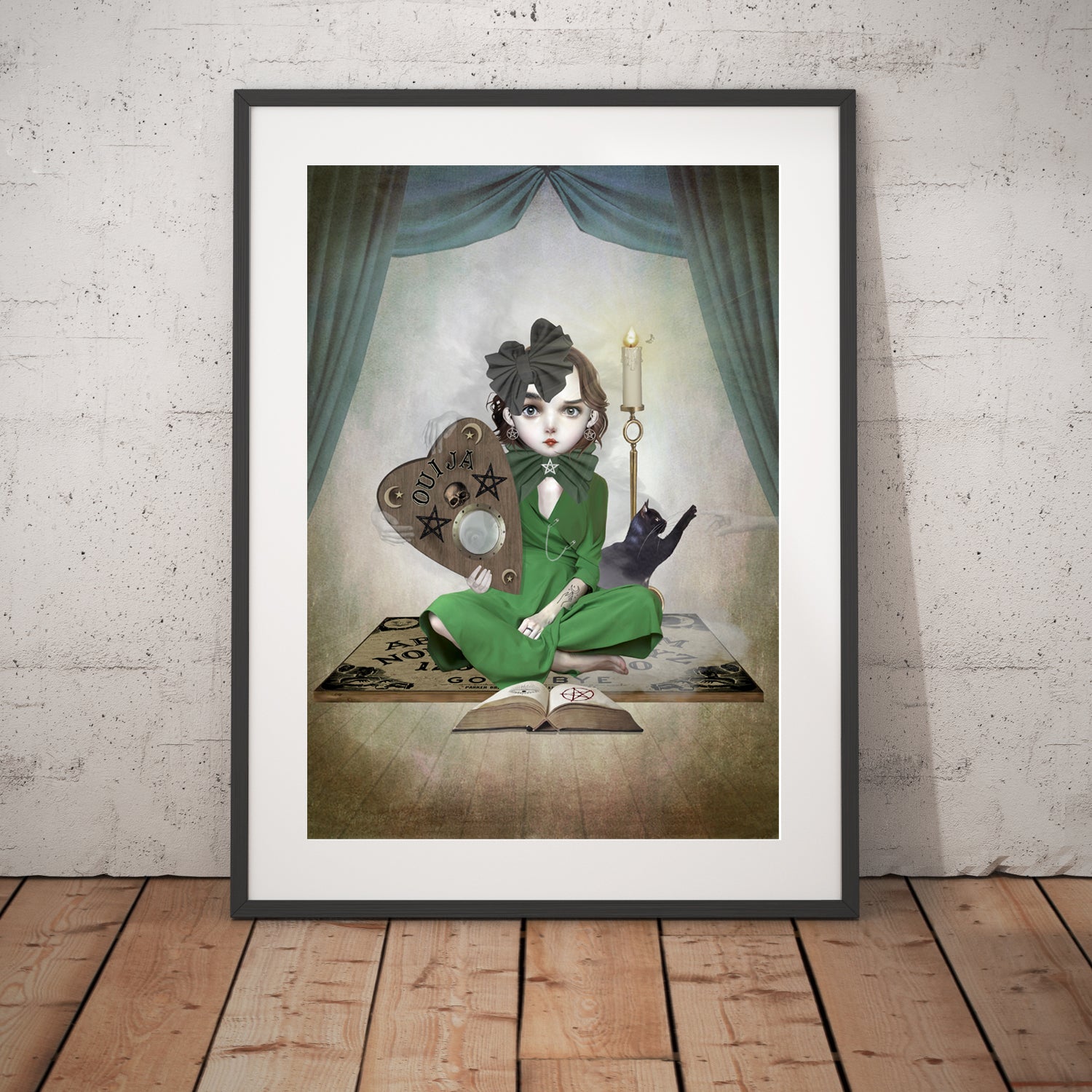 Girl and ouija board art print in a black frame, standing against a white wall.