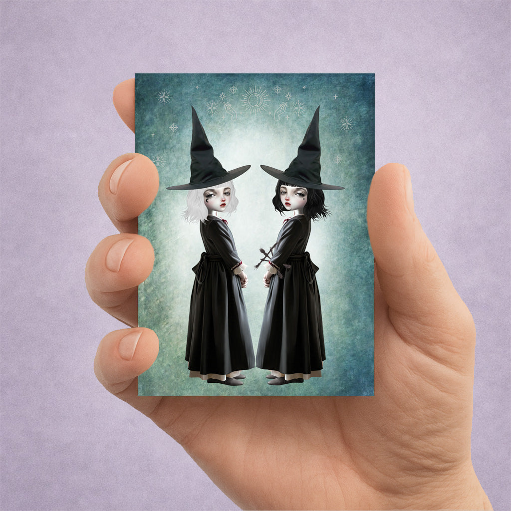 Miniature 2.5x3.5 ACEO art card held in hand, featuring twin gothic witches with white and black hair against a celestial teal background.