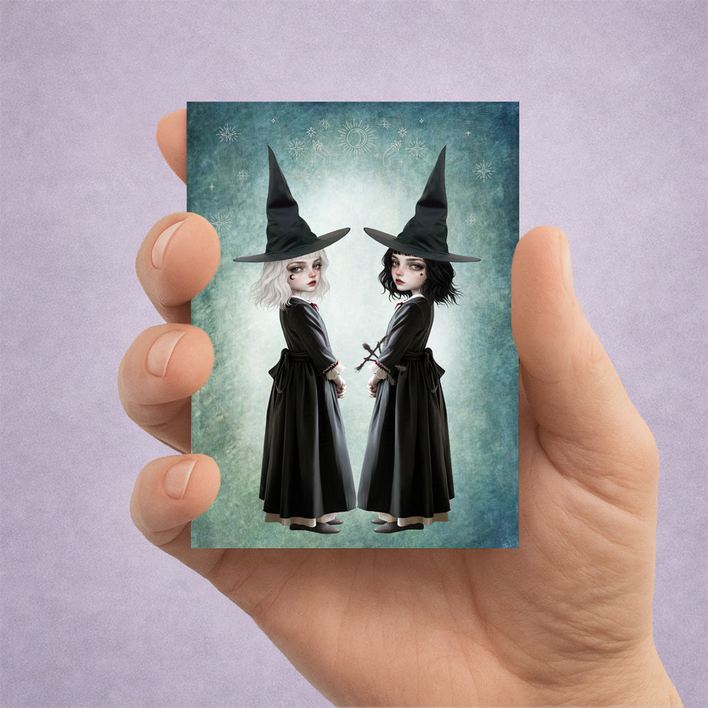 Miniature 2.5x3.5 ACEO art card held in hand, featuring twin gothic witches with white and black hair against a celestial teal background.