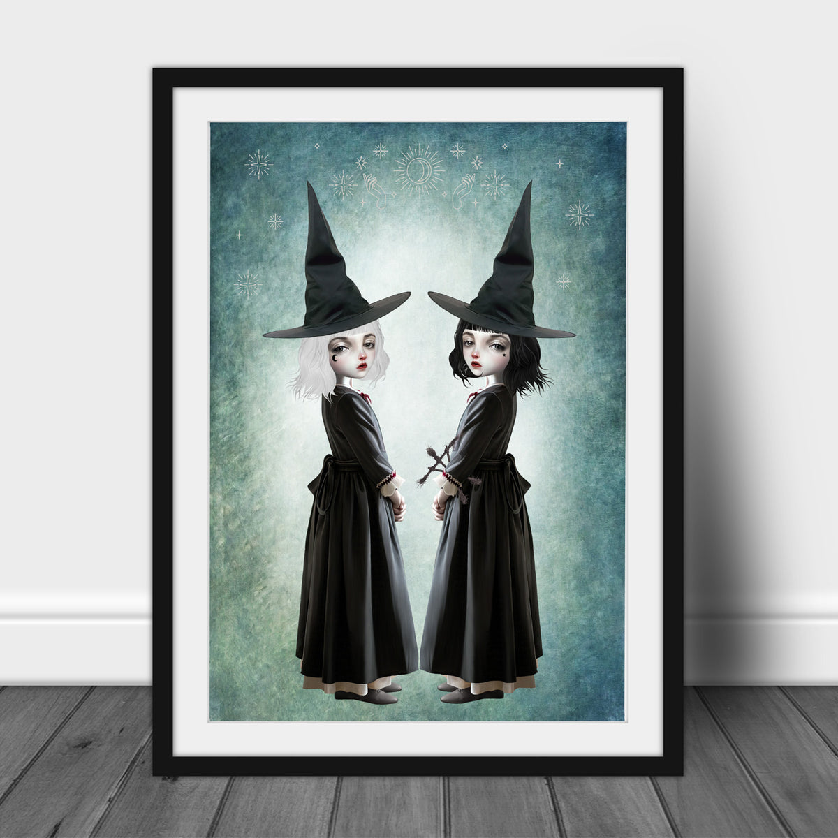 Dark cottagecore fine art print in an A3 frame featuring twin gothic witches with white and black hair wearing pointed hats, set against a celestial teal background.