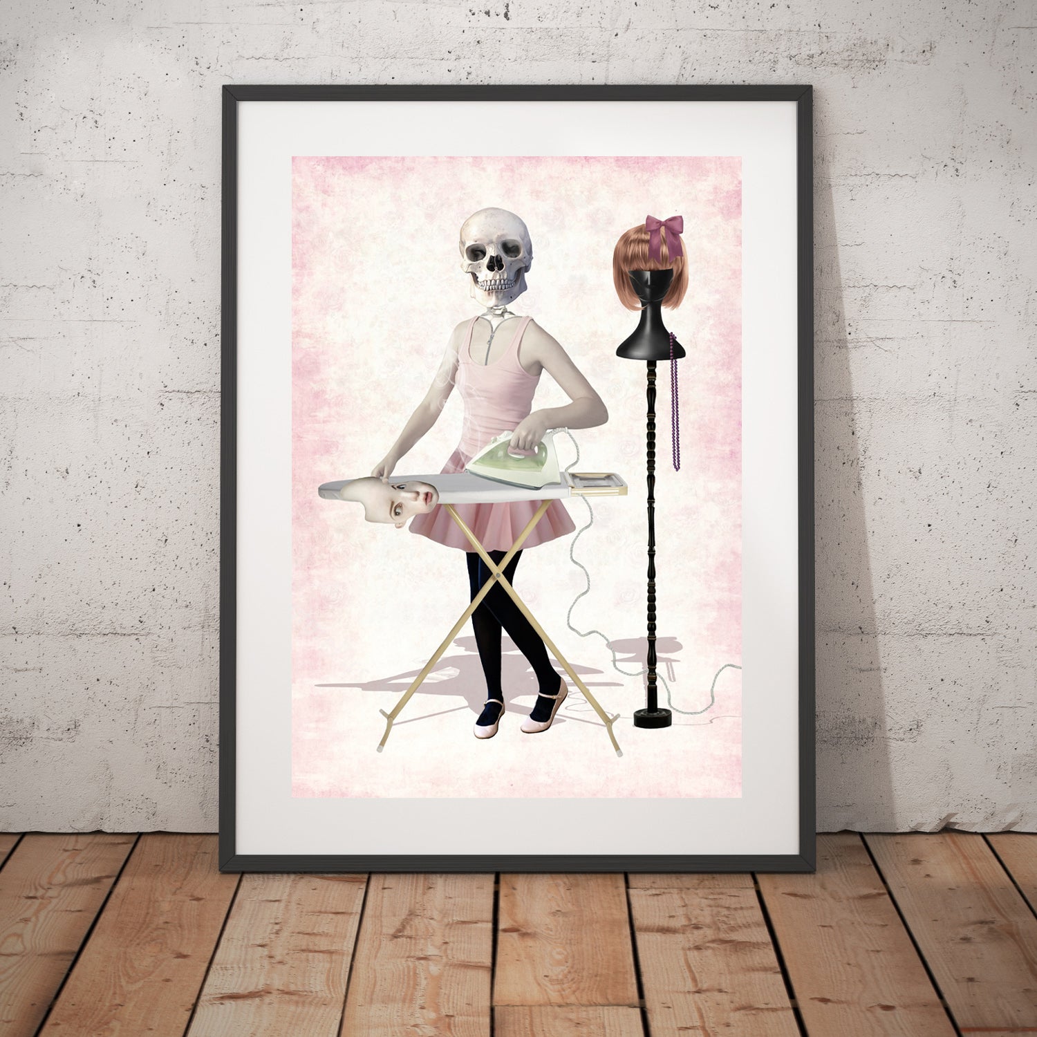 Skeleton girl art print in a black frame, standing against a white wall.