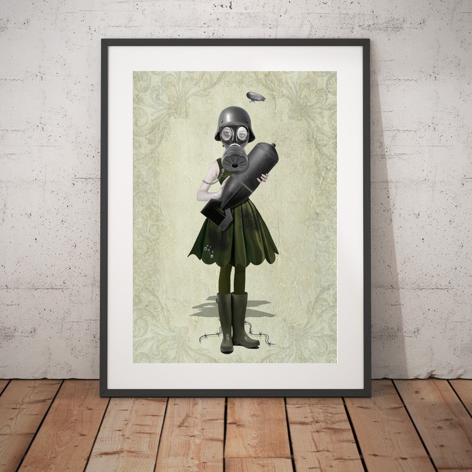 Soldier Girl and bomb art print in a black frame, standing against a white wall.