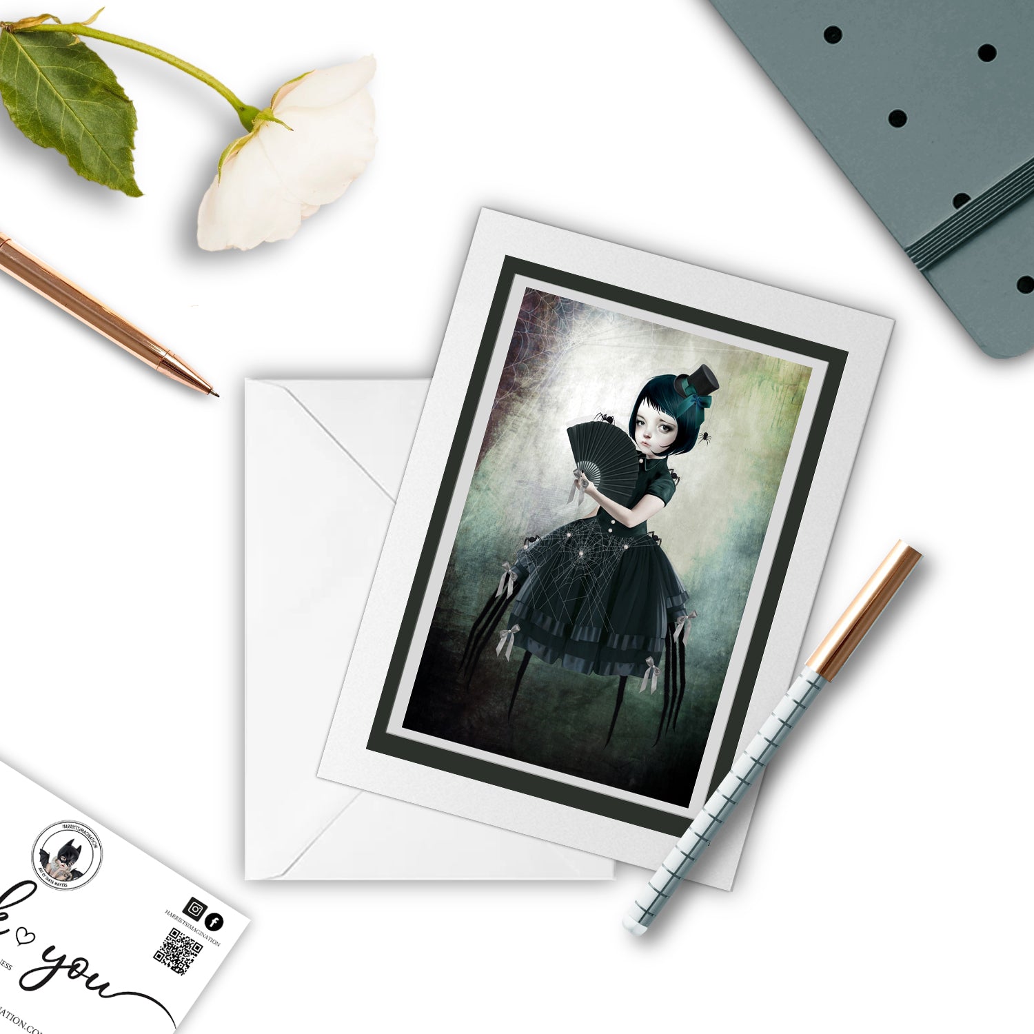 Spider girl art greeting card, with a pen and other stationary items arranged around it.