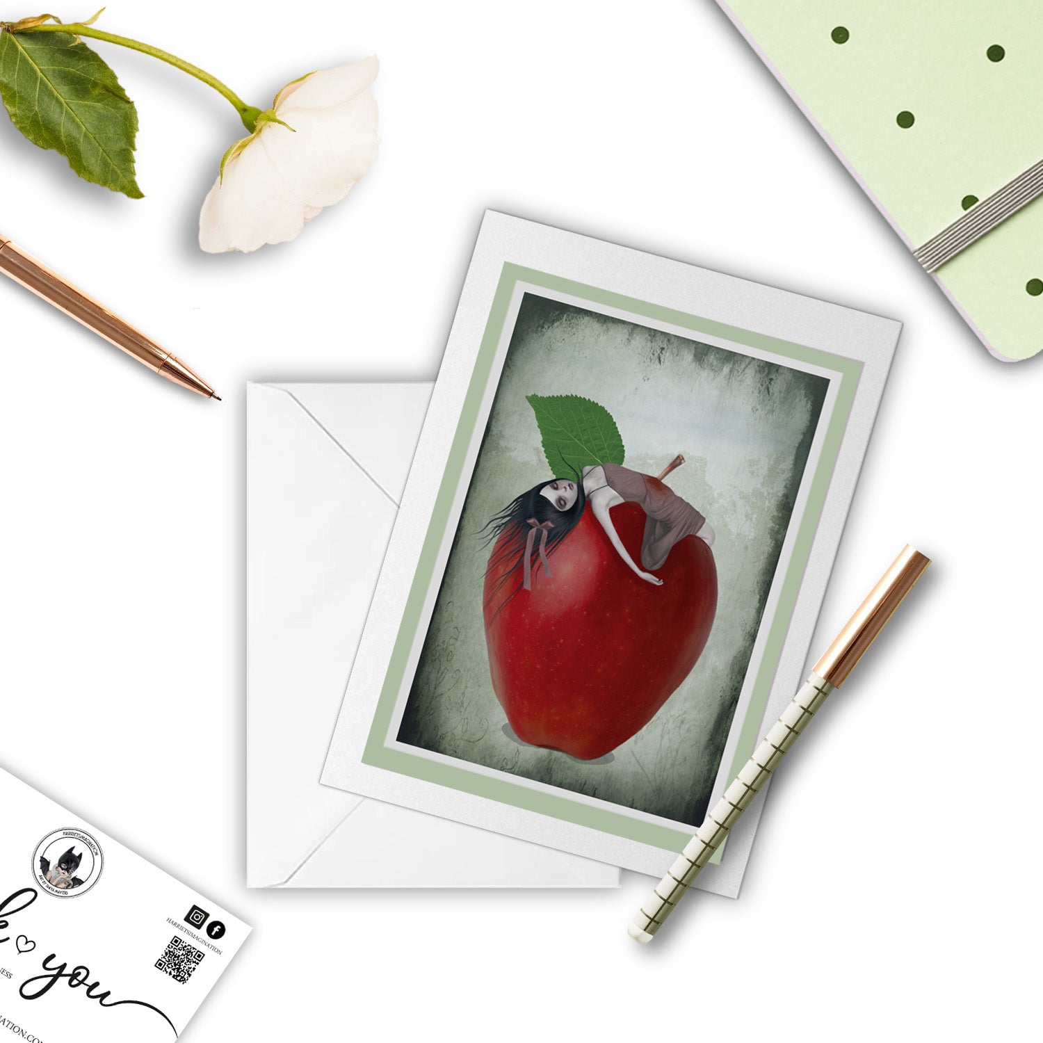 Surreal Red Apple Art Greeting Card with pen and other stationary arranged around it.