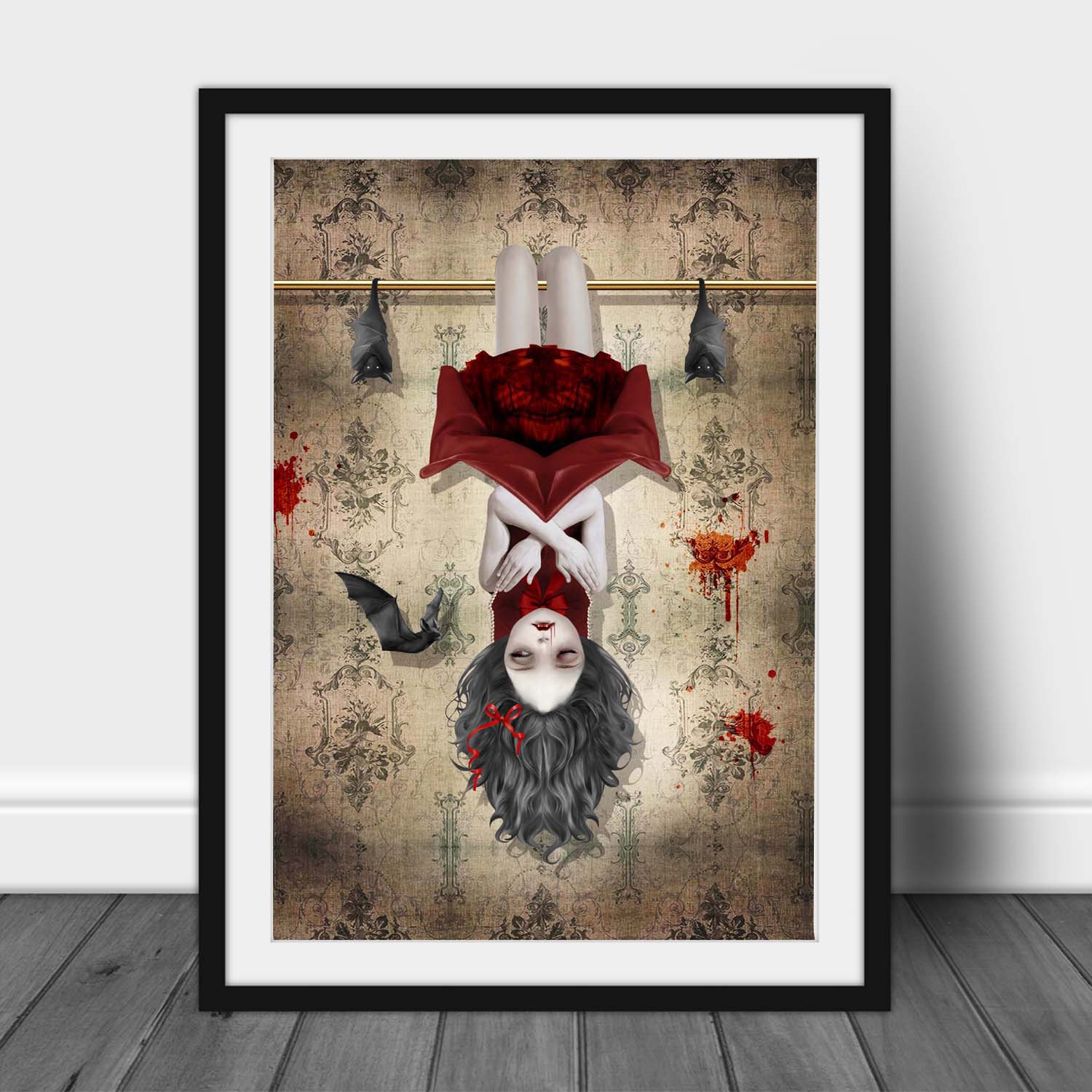 Framed gothic vampire girl and bats wall art leaning against a wall with vintage wallpaper details and dark whimsigoth styling.