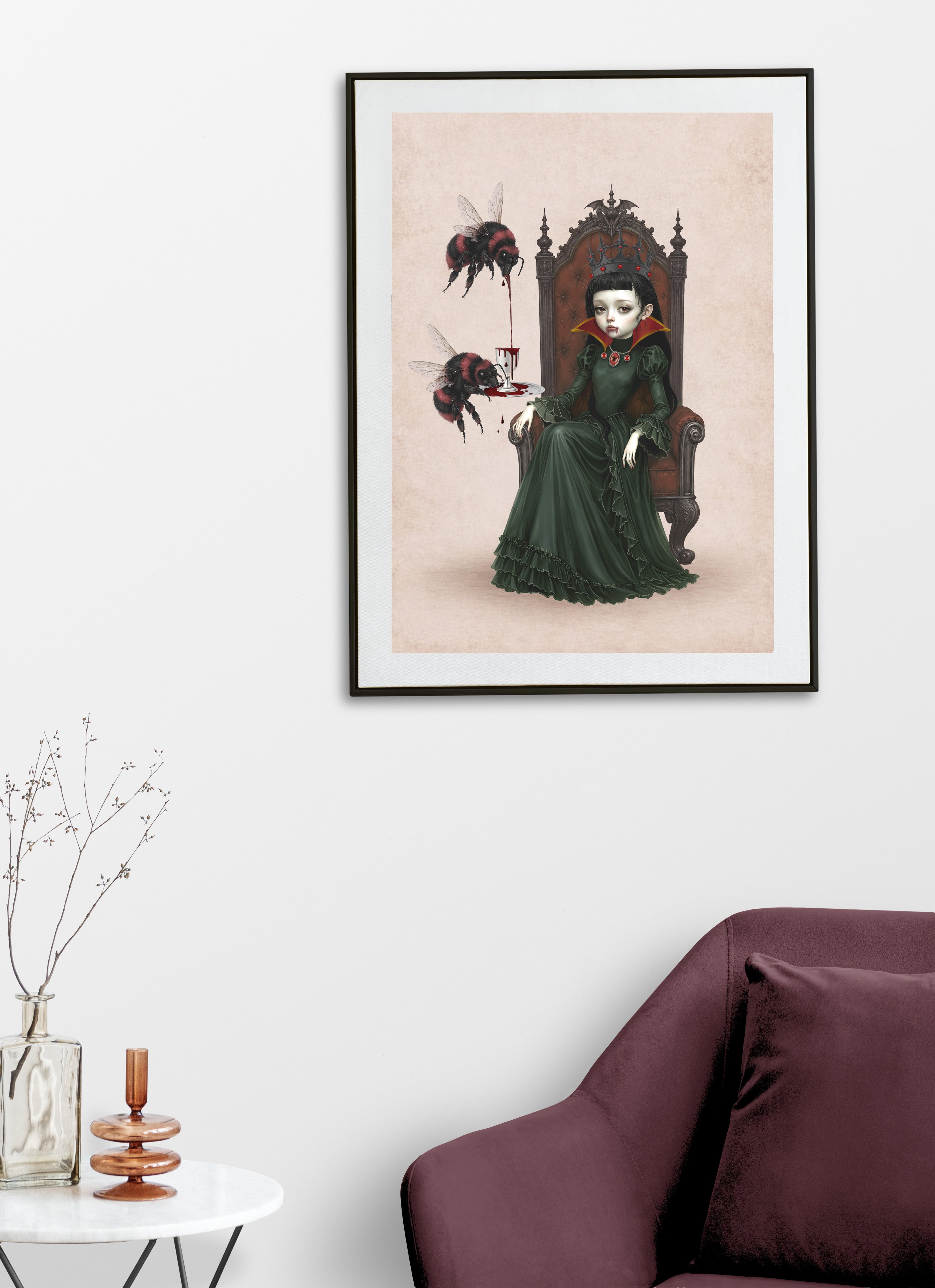 Gothic pop surrealism art print displayed on living room wall, featuring a vampire queen with a black crown sitting on a throne, with two large red-and-black bumblebees pouring blood from a goblet