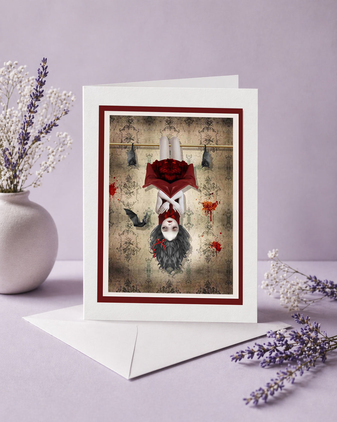 Greeting card with a surreal design of a vampire girl and bats hanging upside down, surrounded by flowers on a light purple background.