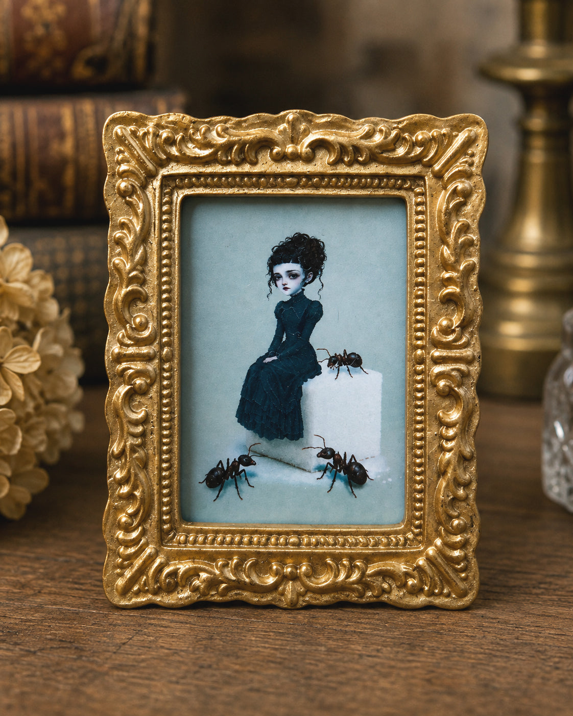 Miniature 1:12 scale gothic art print in an ornate gold frame depicting a pale Victorian woman in a black dress sitting on a sugar cube surrounded by giant ants, displayed in a dollhouse setting.