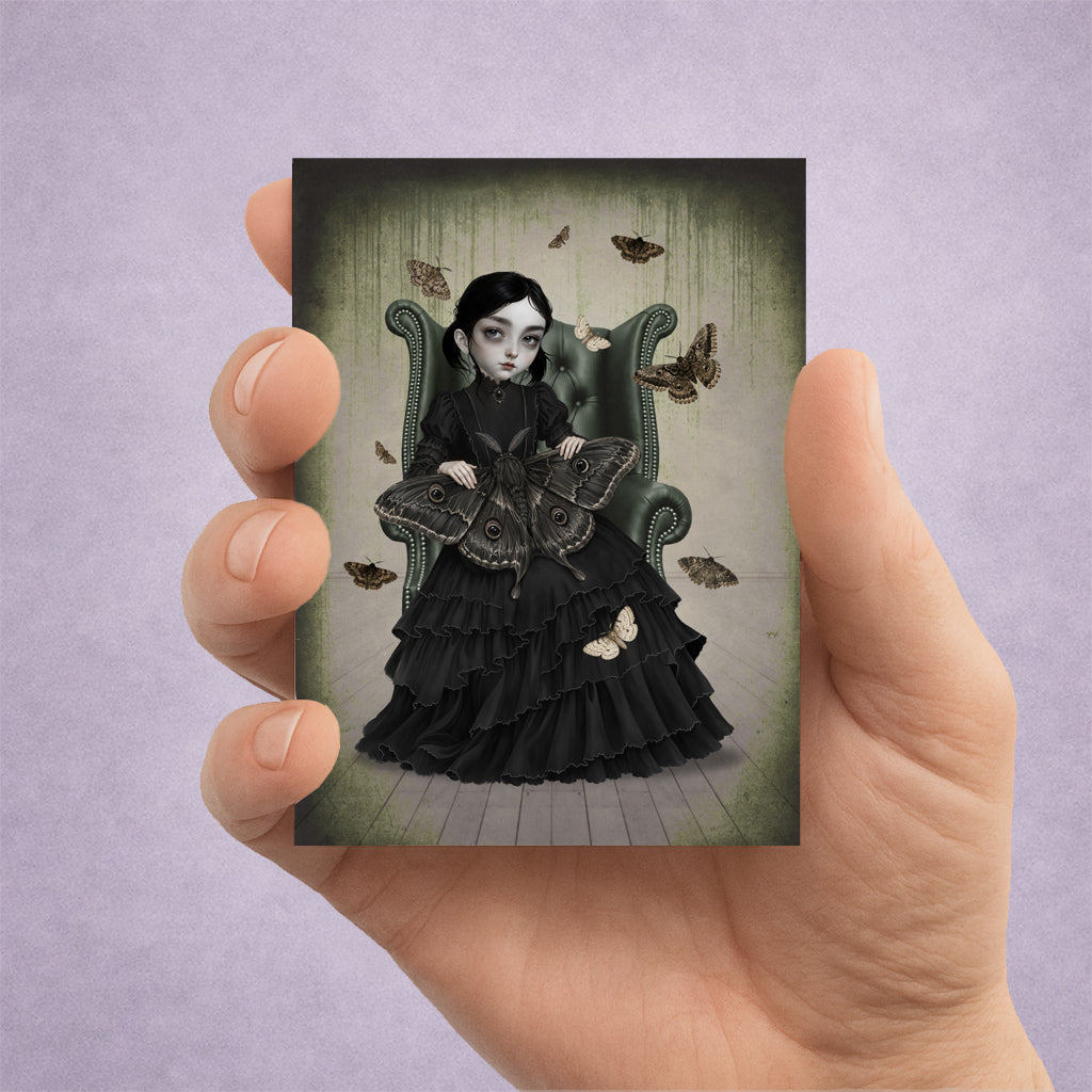 Hand holding a 2.5x3.5 inch ACEO art trading card featuring a gothic girl in a black Victorian dress sitting in an armchair with giant moths.