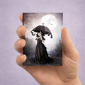 Collectible gothic ACEO art print held in hand featuring a miniature dark fantasy illustration of a girl with bats under a full moon.