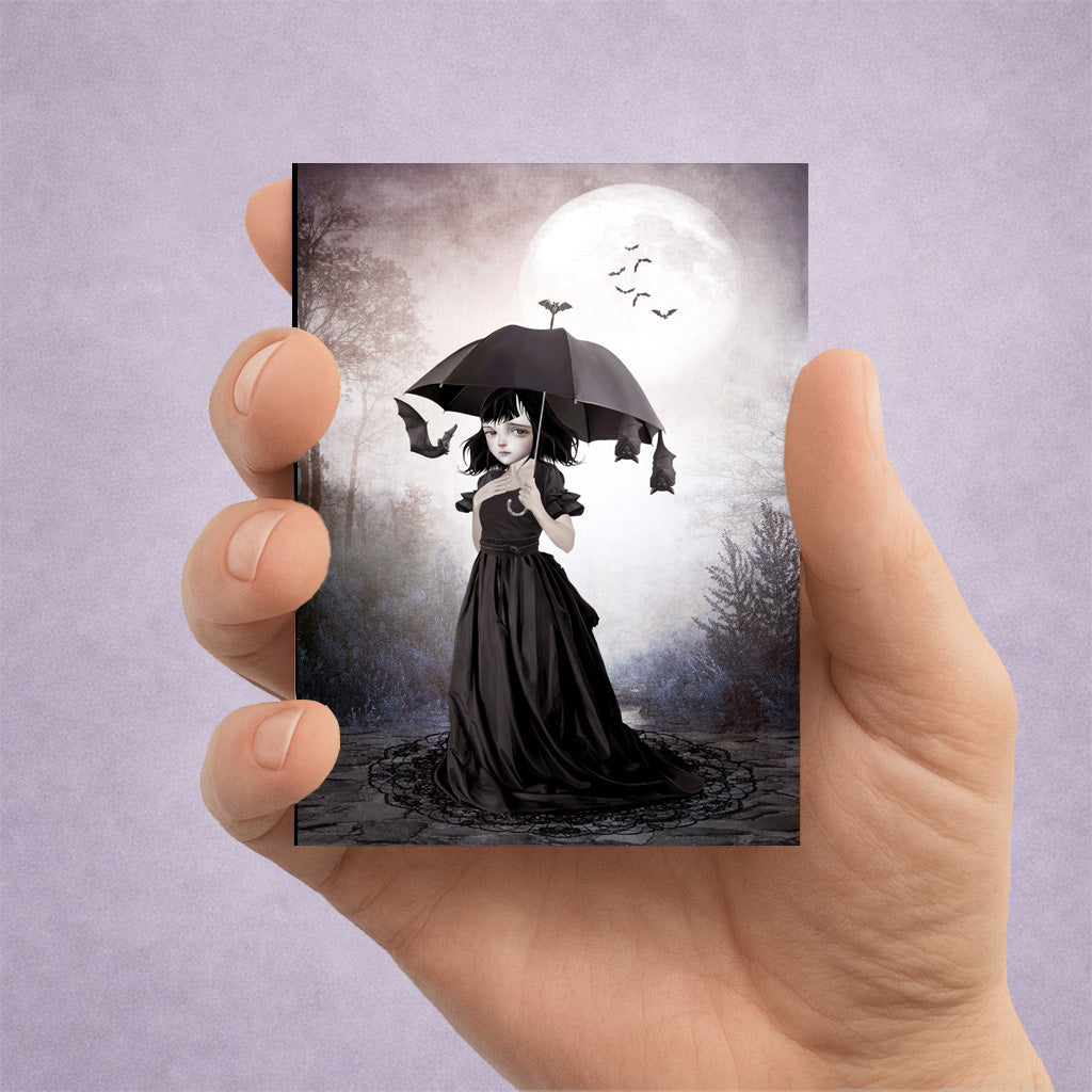 Collectible gothic ACEO art print held in hand featuring a miniature dark fantasy illustration of a girl with bats under a full moon.