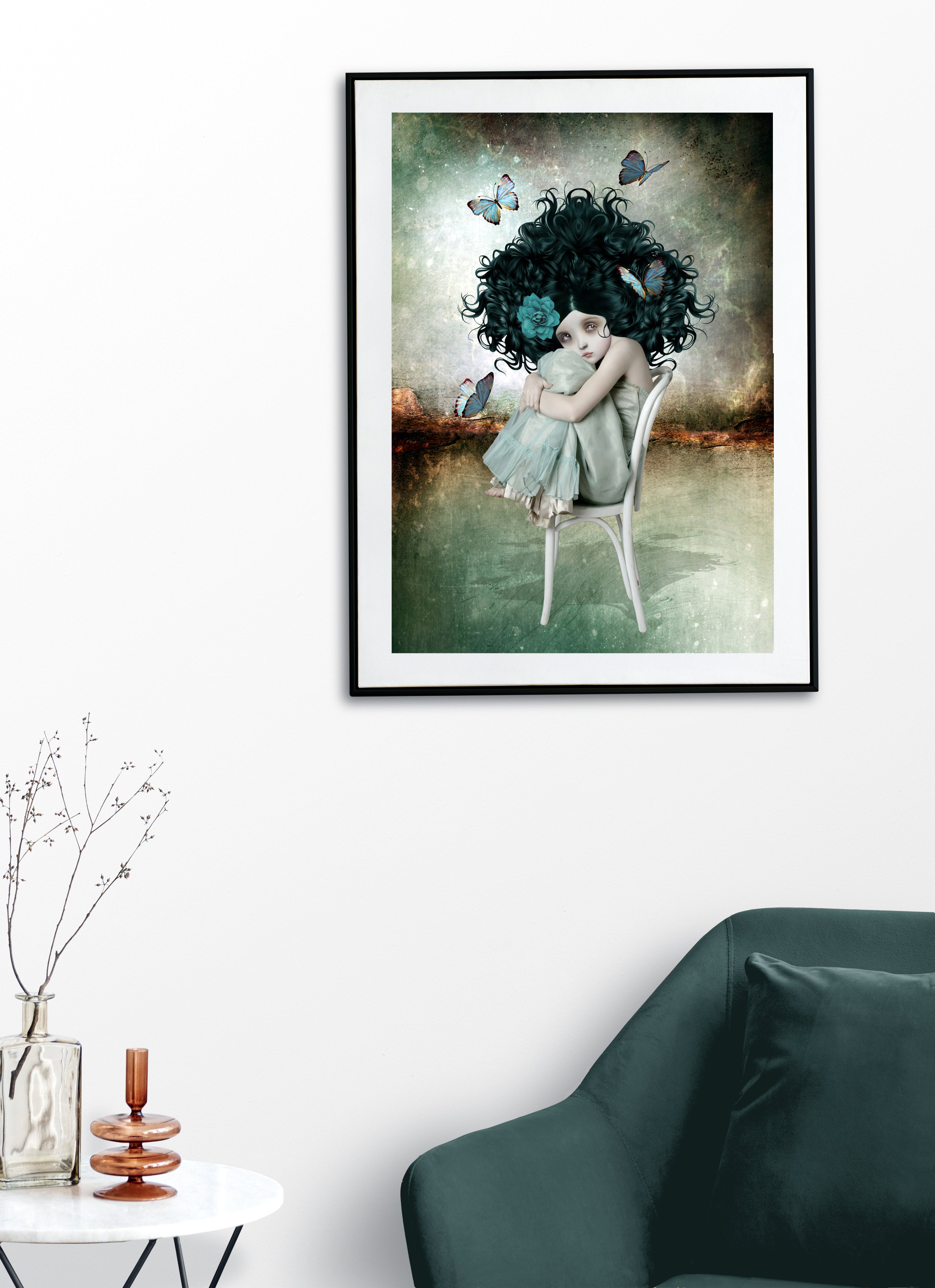 Framed artwork of a woman with dark hair and butterflies in a room with a green sofa and decorative items.