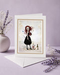 Frameable blank art greeting card titled Whimsical Love Archer standing upright next to a white envelope and lavender flowers, featuring a Pop Surrealism illustration of a gothic redhead archer holding an anatomical heart.