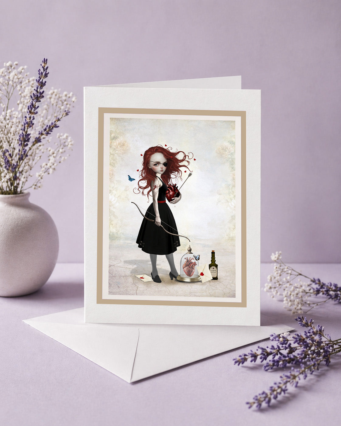 Frameable blank art greeting card titled Whimsical Love Archer standing upright next to a white envelope and lavender flowers, featuring a Pop Surrealism illustration of a gothic redhead archer holding an anatomical heart.