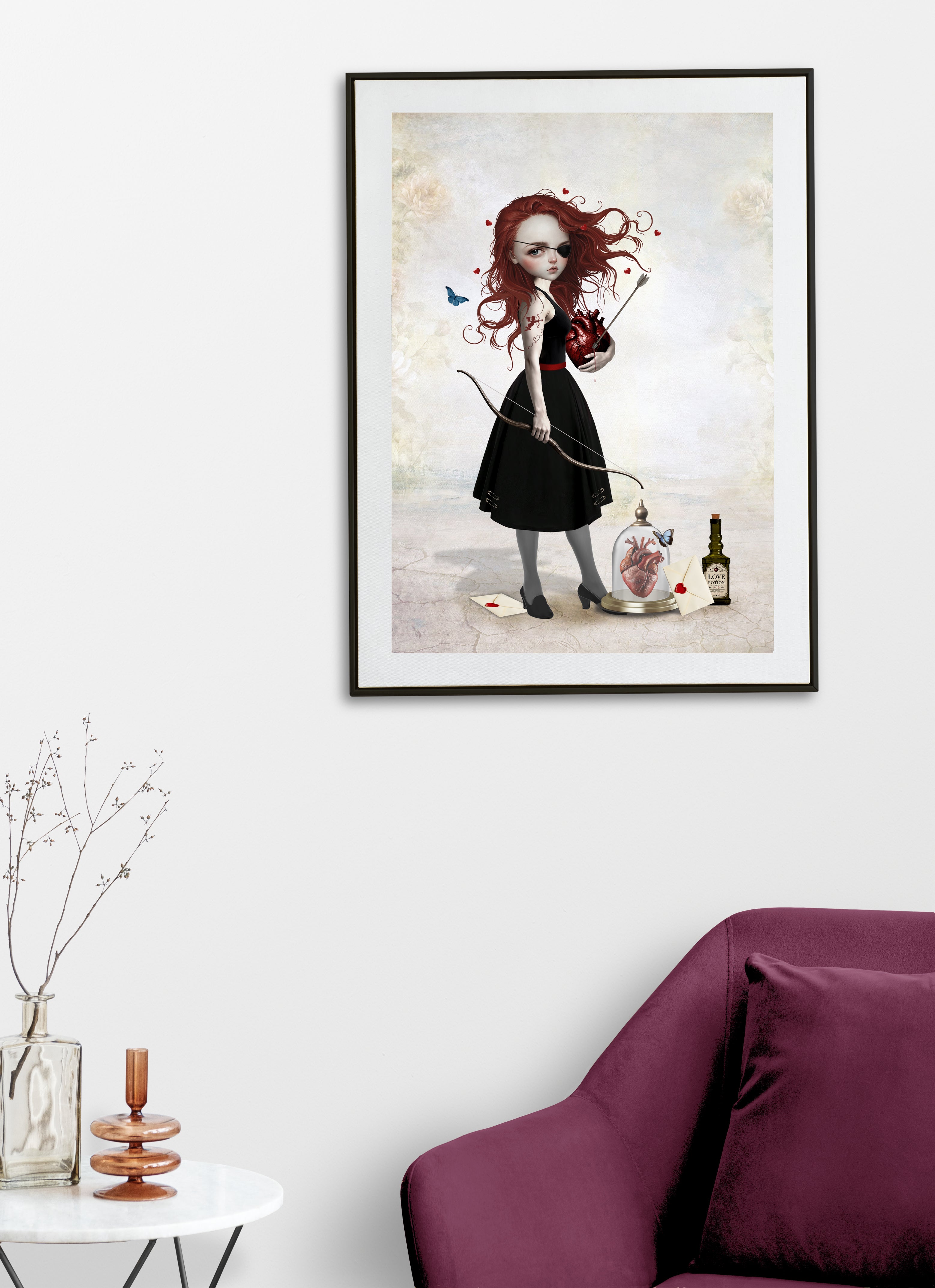 Pop Surrealism art print displayed on a living room wall featuring a redhead girl with an eye patch holding a bow and arrow and a bleeding anatomical heart, alongside a love potion bottle.