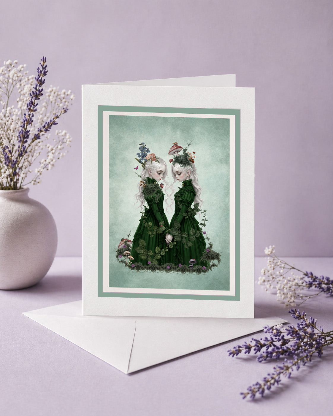 A blank dark cottagecore art greeting card featuring ethereal twin girls, displayed next to a white envelope and lavender sprigs, perfect as a ready to frame miniature print.