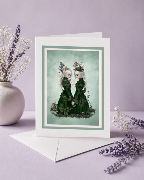 A blank dark cottagecore art greeting card featuring ethereal twin girls, displayed next to a white envelope and lavender sprigs, perfect as a ready to frame miniature print.