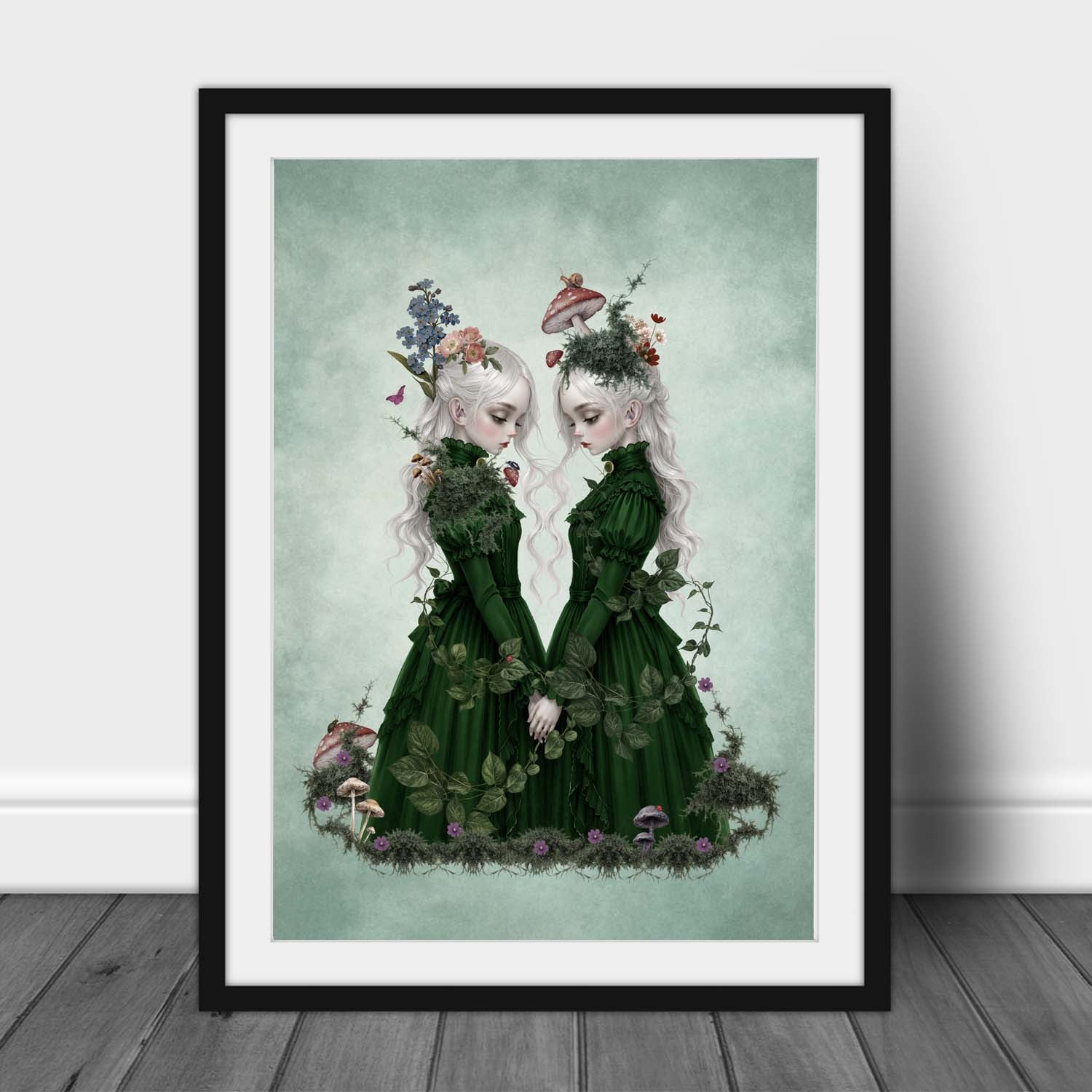 An A3 Framed Art print features two ethereal twin girls with long white hair wearing dark green Victorian dresses, holding hands amidst moss, mushrooms, and forget-me-nots in a dark cottagecore fantasy art print.