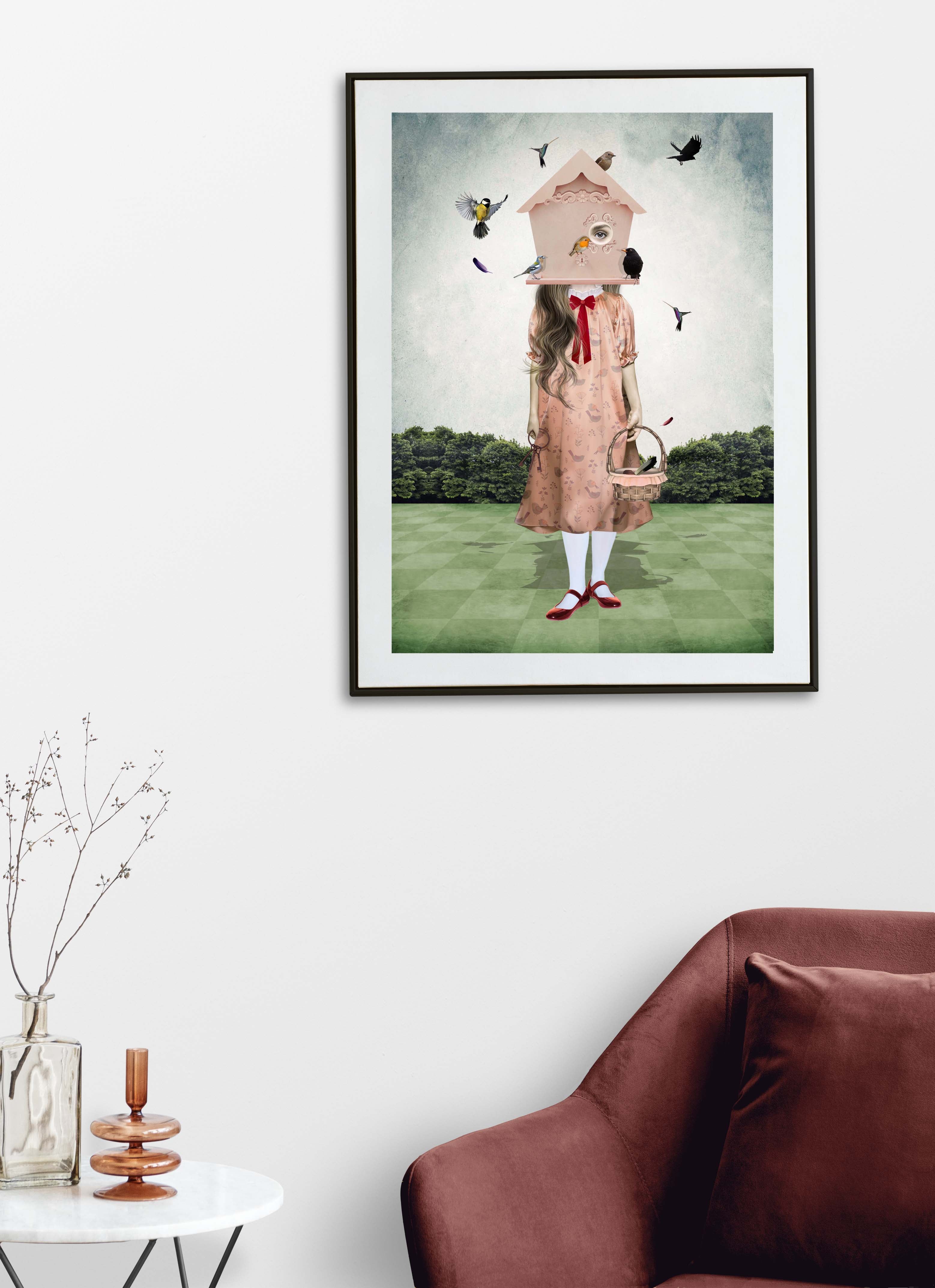 Surreal Birdhouse Girl art print framed on a wall above a wooden table and chair display.