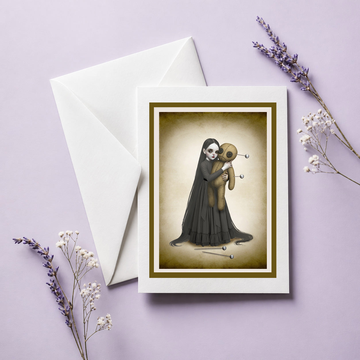 Greeting card with a illustration of a goth girl holding an oversized voodoo doll, accompanied by a white envelope on a light purple background.